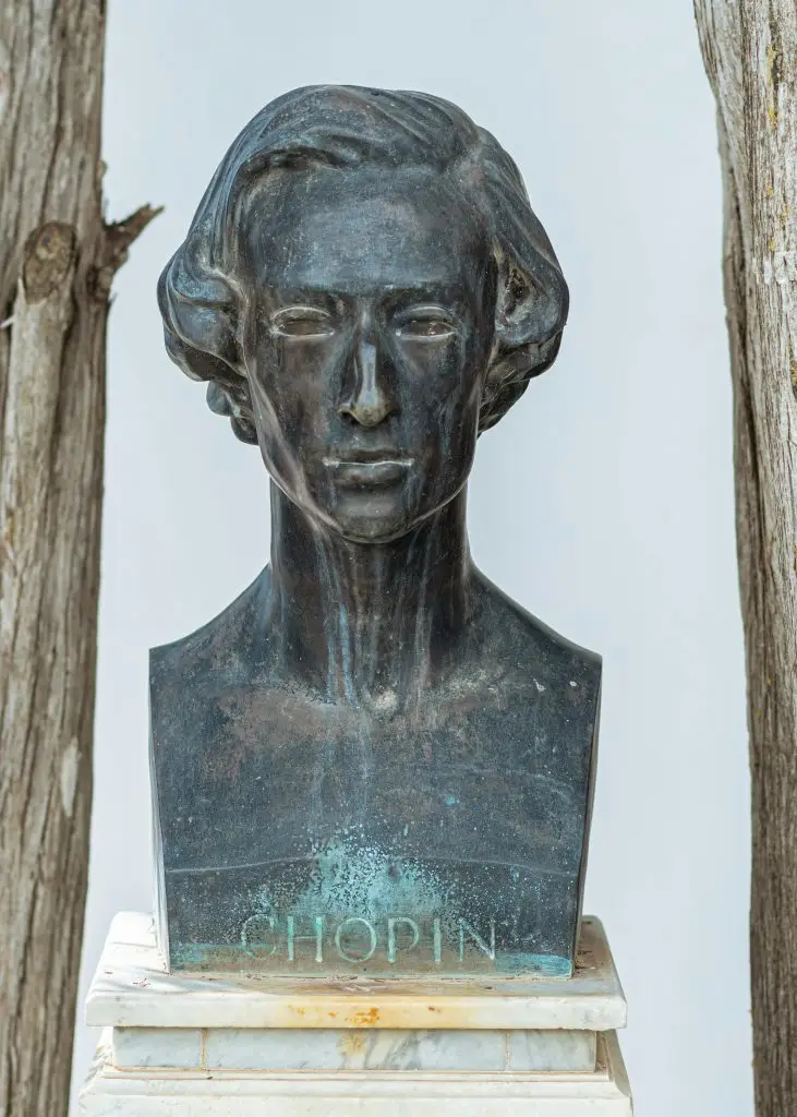 A timeless bronze sculpture of Chopin displayed outdoors with rustic elements.